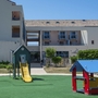 Spielplatz mit Rutsche und Spielhäusern vor einem Gebäude.