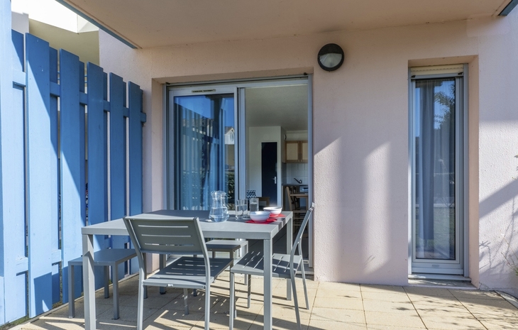 Terrasse mit Tisch und Stühlen vor einem Gebäude mit Glas- und Holzelementen.