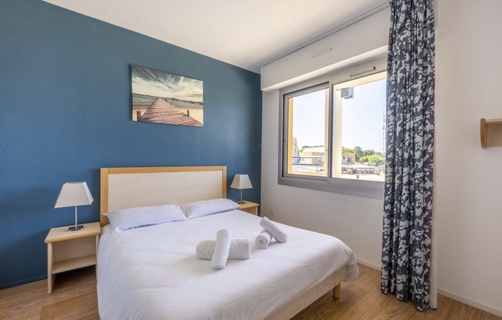 Helles Schlafzimmer mit Doppelbett, Fenster und Wandbild.