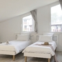 Zwei Einzelbetten in einem hellen Gästezimmer mit Dachfenster und Kommode.