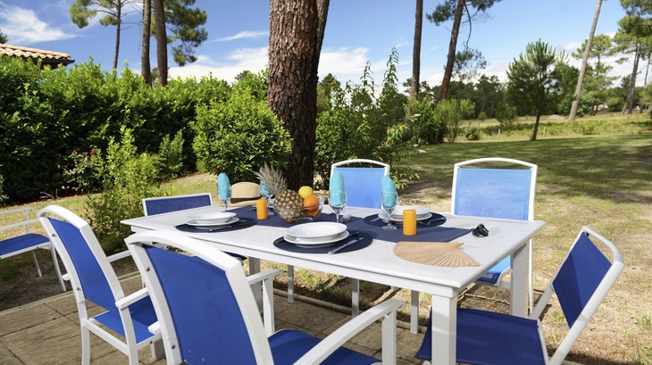 Gartentisch mit blauen Stühlen, gedeckt für ein Essen im Freien, umgeben von Bäumen.