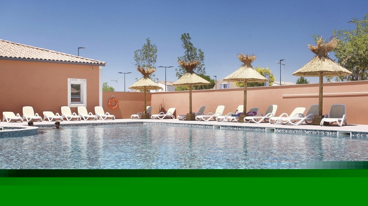 Pool mit Liegestühlen und Sonnenschirmen vor rosa Gebäuden im Freien.