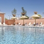 Pool mit Liegestühlen und Sonnenschirmen vor rosa Gebäuden im Freien.