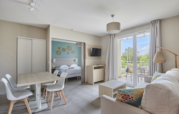 Wohnzimmer einer Ferienwohnung mit Sofa, Esstisch und Blick auf Terrasse und Garten.