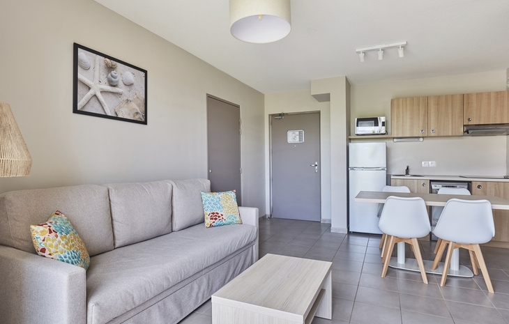 Helles Wohnzimmer mit Sofa, Küchenzeile und Essbereich in modernem Apartment.