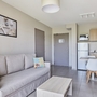 Helles Wohnzimmer mit Sofa, Küchenzeile und Essbereich in modernem Apartment.