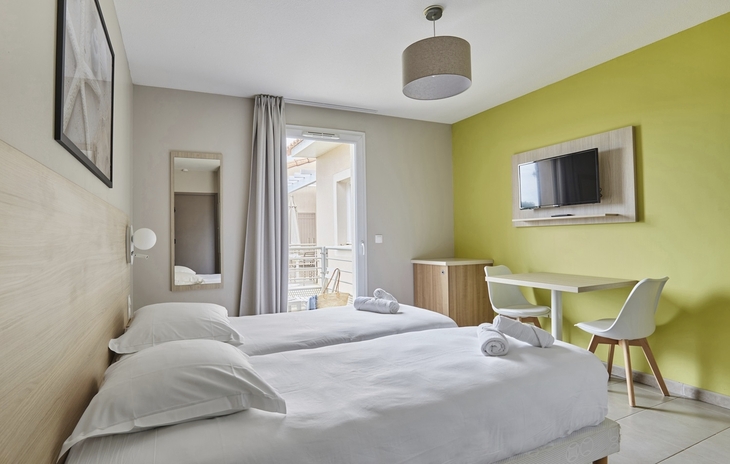 Helles Hotelzimmer mit zwei Einzelbetten, Schreibtisch und Flachbildfernseher.