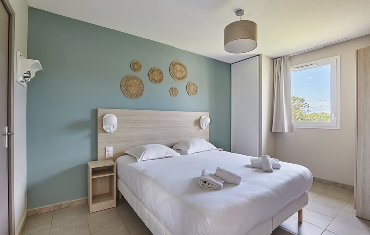 Helles Schlafzimmer mit Doppelbett, Handtüchern und dekorativen Wandkörben.