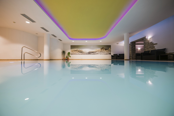 Hallenbad mit beleuchteter Decke und Wandbild in einem modernen Spa-Bereich.