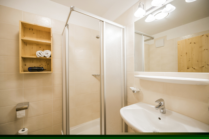 Helles Badezimmer mit Dusche, Waschbecken und Spiegel im Hotel Alpenrose.