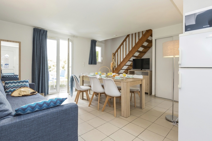 Wohnzimmer mit Esstisch, Sofa, Treppe und Glastüren in einem Ferienhaus.
