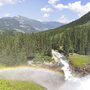 Krimmler Wasserfälle im Nationalpark Hohe Tauern mit Regenbogen in bewaldeter Bergkulisse.