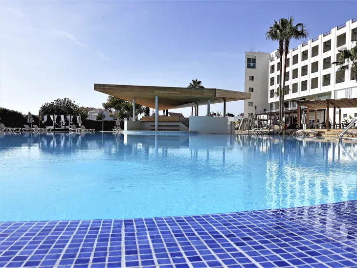 Hotelpool mit Sonnenschirmen und Palmen bei klarem Himmel.