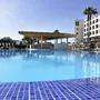Hotelpool mit Sonnenschirmen und Palmen bei klarem Himmel.