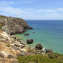 Küste mit Klippen und blauem Meer unter klarem Himmel.