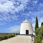 Windmühle in Vila Real, Algarve, umgeben von Flora und blauem Himmel.