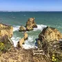 Küste der Algarve in Portugal mit Blick auf Felsen im Meer und blauem Himmel.