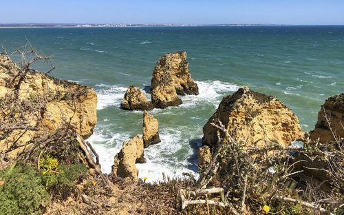 Küste der Algarve in Portugal mit Blick auf Felsen im Meer und blauem Himmel.
