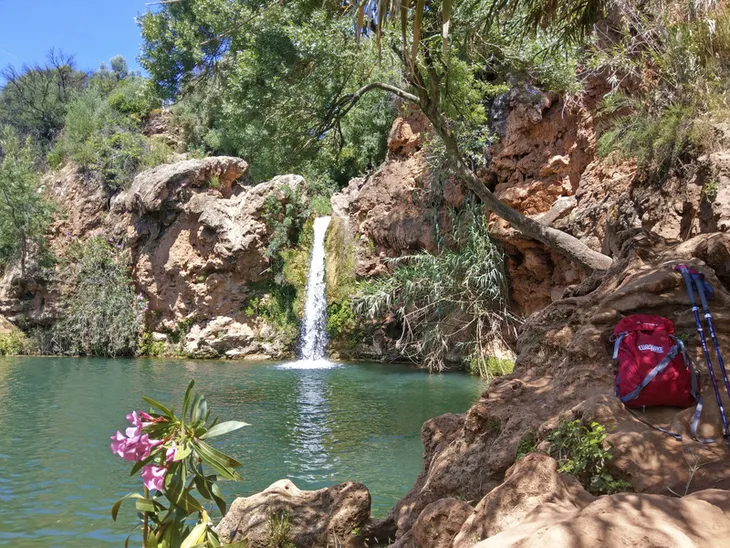 Wasserfall Pego do Inferno in Portugal mit Rucksack und Wanderstöcken im Vordergrund.