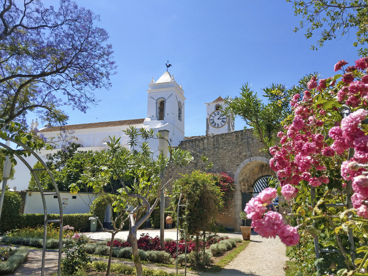 Garten, Blumen und Kirche unter blauem Himmel in Tavira, Algarve.