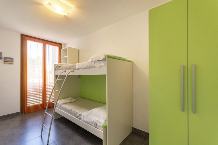Zimmer mit Etagenbett, grünem Schrank und großem Fenster.