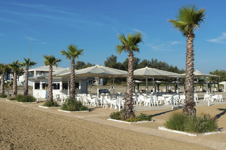 Strandcafé mit Palmen auf der Isola di Albarella bei sonnigem Wetter.