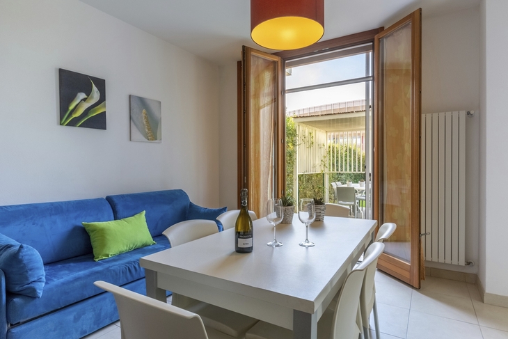 Wohnraum mit blauem Sofa, Esstisch und offener Balkontür.