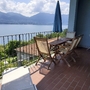 Terrasse mit Tisch, Stühlen und Schirm, Blick auf See und Berge im Hintergrund.