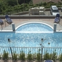Zwei Personen schwimmen in einem rechteckigen Pool mit Pflanzenumrandung.