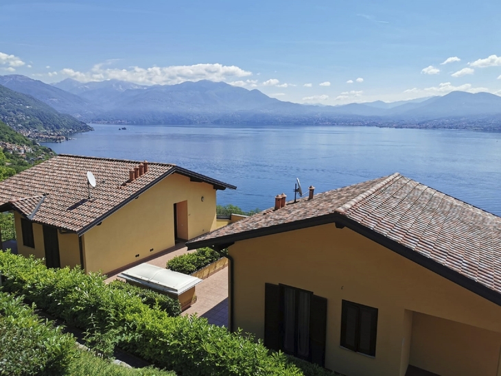 Gelbes Haus mit Terrakottadach, Blick auf See und Berge im Hintergrund.