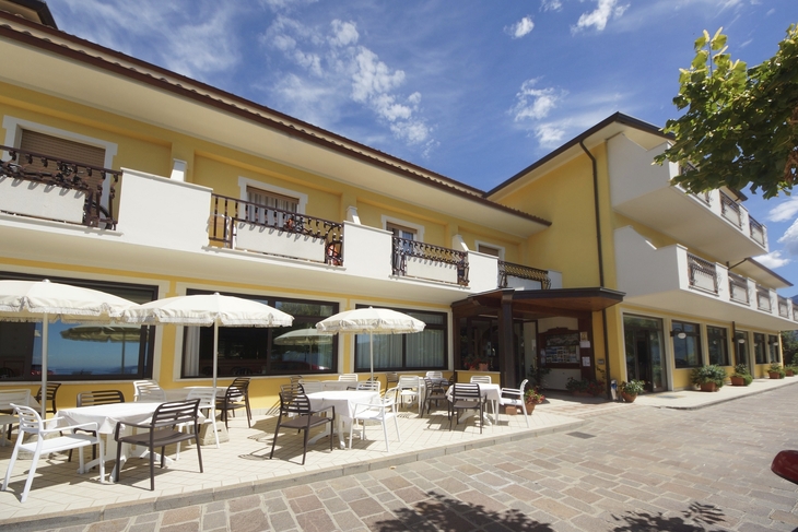 Außenansicht eines gelben Hotels mit Terrasse und Sonnenschirmen.