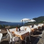 Pizzeria-Terrasse mit Seeblick, Tische, Stühle und Sonnenschirme unter blauem Himmel