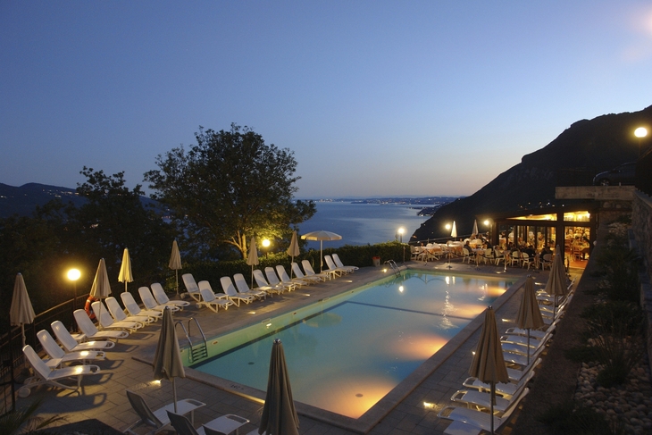 Pool bei Nacht mit beleuchteter Pizzeria und Bergblick.