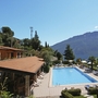Außenansicht der Residence La Rotonda, Pool, Sonnenschirme, Berge und See im Hintergrund.