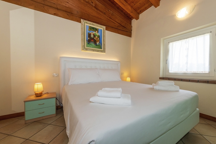 Schlafzimmer mit Doppelbett, Holzdecke und Wandbild, hell beleuchtet.