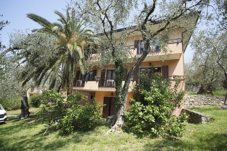 Ein dreistöckiges Haus mit Balkon, umgeben von Bäumen und grüner Vegetation.
