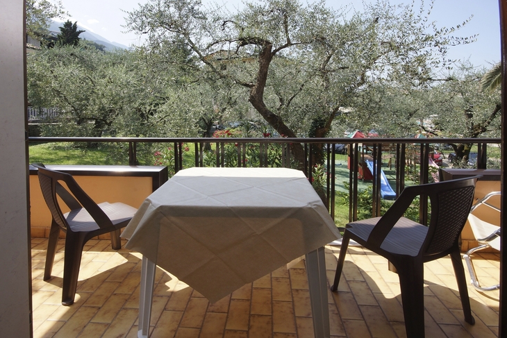 Balkon mit Tisch, zwei Stühlen und Blick auf blühende Bäume.
