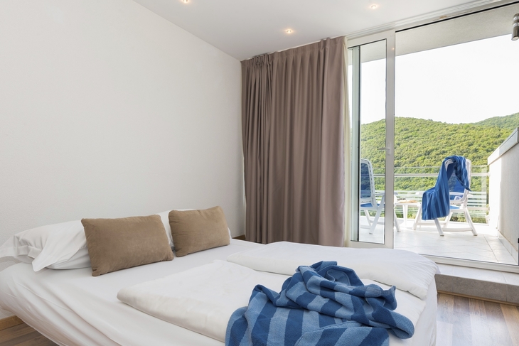 Superior Zimmer mit Balkon, Blick auf grüne Hügel, Bett mit blauen Decken.