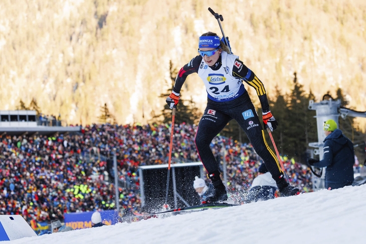 Biathlet im Rennen des Staffelwettbewerbs mit verschneiter Berglandschaft im Hintergrund.