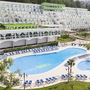 Hotel mit Pool, umgeben von Liegestühlen und grüner Landschaft.