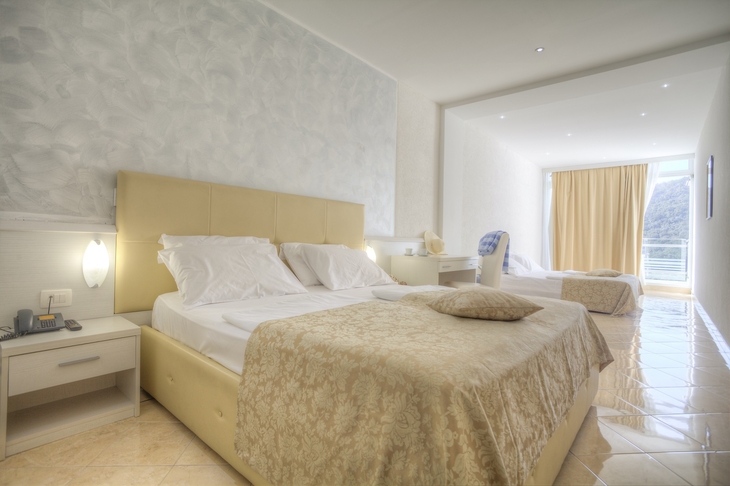 Helles Hotelzimmer mit zwei Betten und Meerblick durch ein großes Fenster.