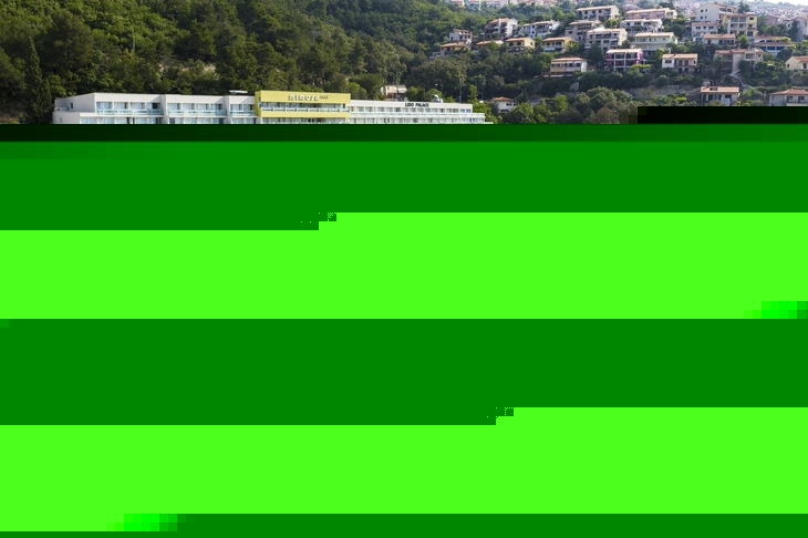 Hotel mit Blick auf Poolbereich und Tennisplatz, umgeben von grüner Landschaft.