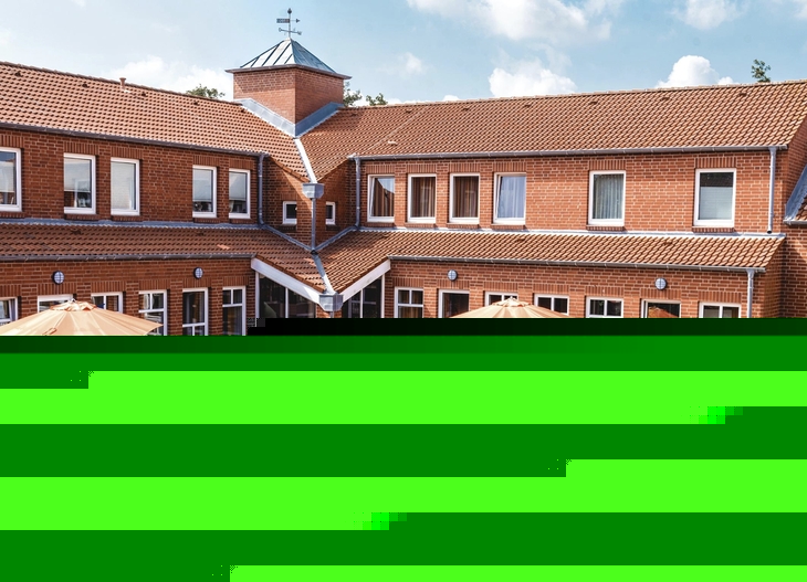 Rotes rechtwinkliges Backsteingebäude der Ferienanlage Büsum mit Terrasse, Sitzmöbeln und Sonnenschirmen bei sonnigem Wetter.