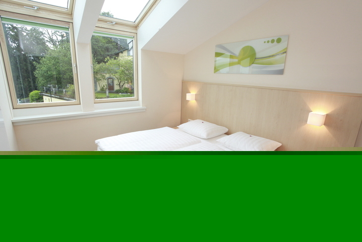 Helles Schlafzimmer in der Ferienanlage Lindau, im Haus an der Obstwiese, mit Doppelbett mit Lampen, senkrechten Fenstern und Dachfenstern und einem Bild über dem Bett. .