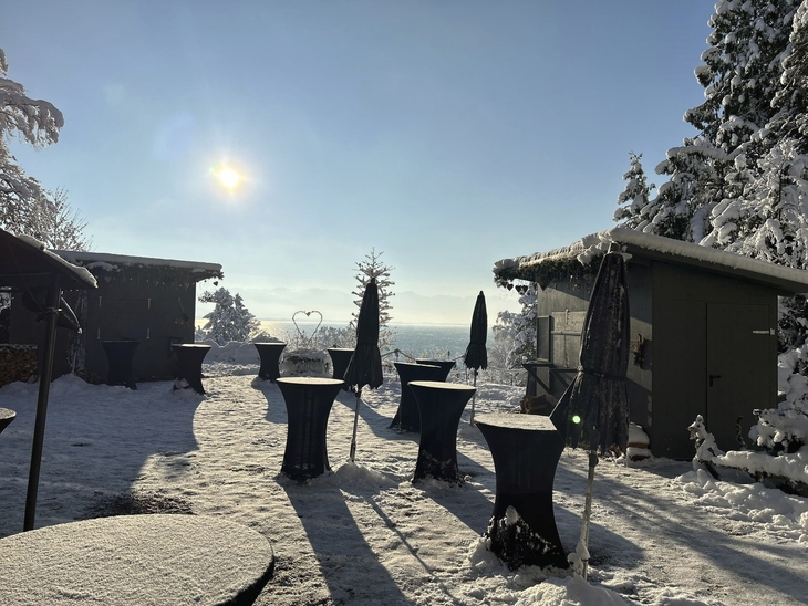 Verschneite Terrasse am Bodensee mit Wintersonne und Hütten im Hintergrund.