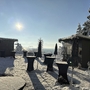 Verschneite Terrasse am Bodensee mit Wintersonne und Hütten im Hintergrund.