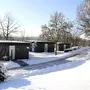 Bungalows der Ferienanlage Prüm in schneebedeckter Winterlandschaft mit Bäumen unter klarem Himmel.