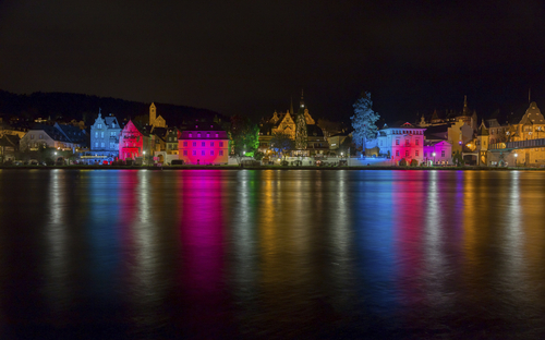 Beleuchtete Häuser am Moselufer bei Nacht, reflektiert im Wasser.