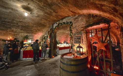 Weihnachtsmarkt in einem Weinkeller mit dekorierten Ständen und Besuchern.