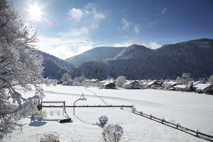 Winterlandschaft in Oberwössen mit schneebedeckten Häusern und Bergen bei Sonnenschein
